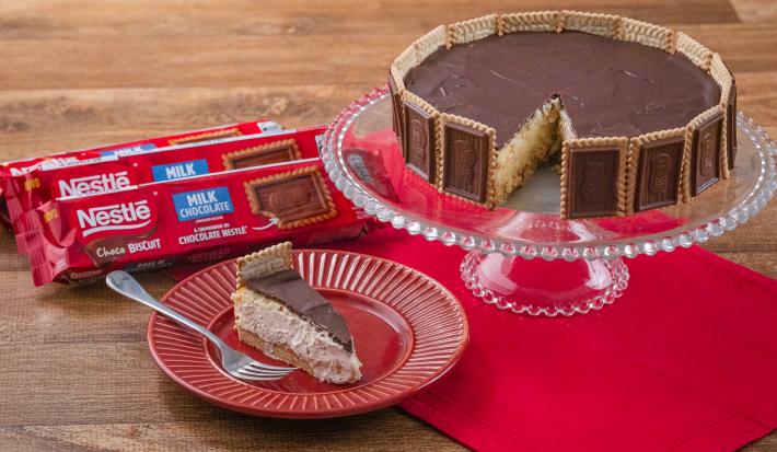 Fotografia em tons de vermelho com uma torta holandesa ao centro feita com Biscoito Choco Biscuit. Ao fundo existe três pacotes de biscoito Choco Biscuit NESTLÉ