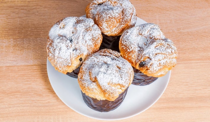 Fotografia mostra um mini panetone em forminha escura, visto de cima, com açúcar de confeiteiro polvilhado.