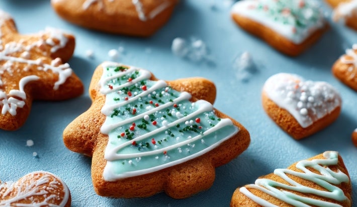 Em cima de uma mesa, biscoitos em forma de boneco de neve,  decorado com glacê branco e verde e confeitos coloridos.