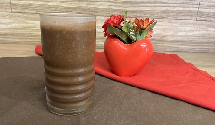 Fotografia em tons de marrom e vermelho com um copo vermelho ao centro. Dentro do copo existe uma bebida feita com suco de maracujá e achocolatado NESCAU, de cor marrom escura.