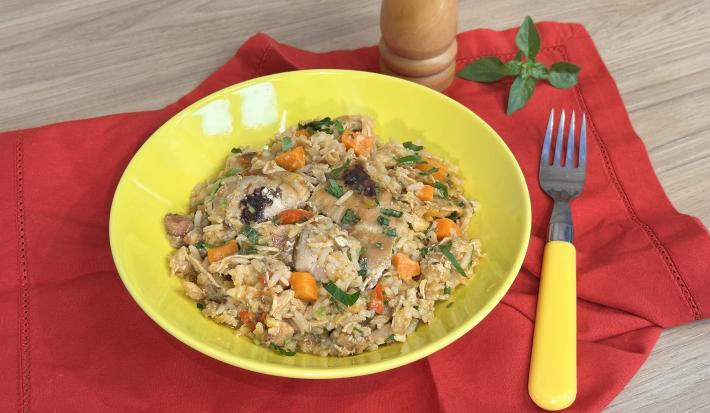 Fotografia em tons de amarelo e vermelho com um prato vermelho ao centro. Dentro do prato existe uma receita de galinhada feita com frango, cenoura e arroz
