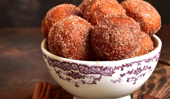 Em cima de uma mesa, tigela com bolinhos redondo, polvilhado com açúcar e canela.