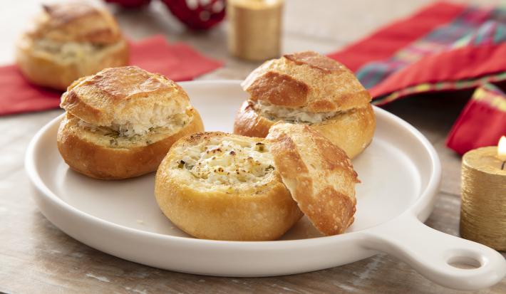 Foto da receita de Pão de Alho na Air Fryer. Observa-se três pãezinhos italianos em um recipiente refratário branco de porcelana, sendo que o da frente está aberto expondo o recheio de queijo.