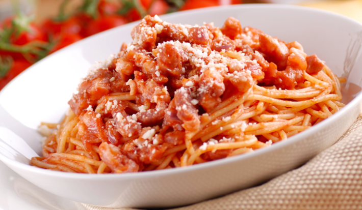 sobre um prato branco, uma porção de macarrão com molho de tomates pedaçudos e queijo ralado.