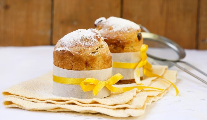 Fotografia mostra um mini panetone em forminha branca, com um laço amarelo em volta.