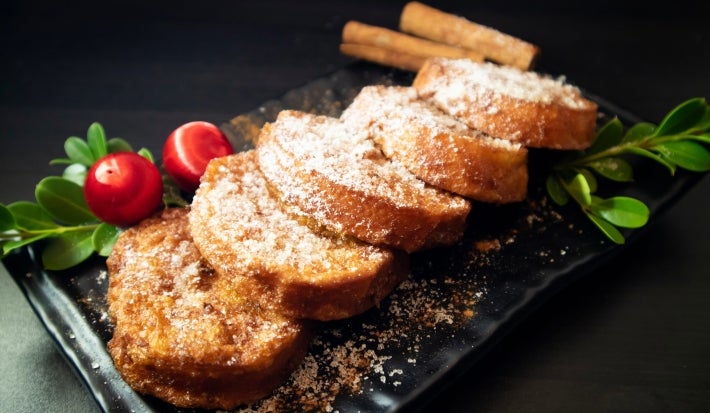Em cima de uma mesa, prato com cinco rabanadas, polvilhadas com açúcar de confeiteiro.