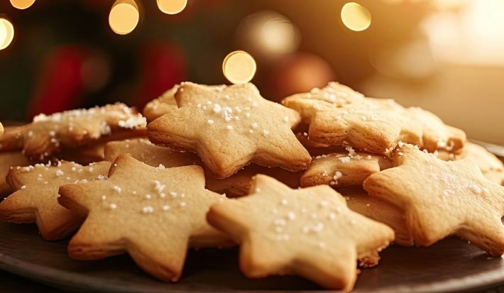 Em cima da mesa, prato com biscoitos crocantes em forma de estrela, decorado confeito branco de bolinhas.