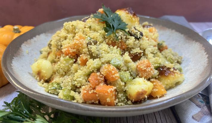 Foto da receita de Cuscuz Marroquino. Observa-se um prato de cerâmica claro redondo contendo a receita finalizada com um ramo de salsa verde.