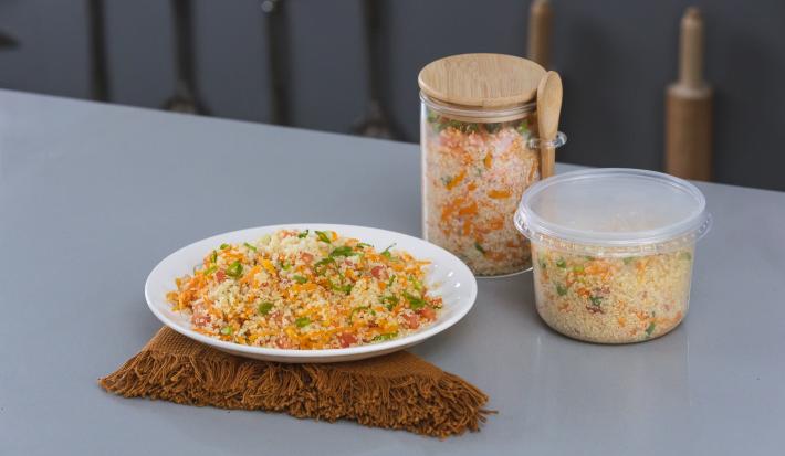 Foto da receita de salada de quinoa, servida em um prato branco, sobre uma tábua, e armazenada em potinhos de varios tamanhos