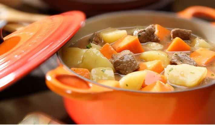 foto tirada de uma panela laranja com pedaços de carne com colorau, batata e abóbora e ao lado a tampa