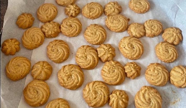 Foto em tons de bege da receita de petit four servida em diversas porções sobre uma forma circular forrada com papel manteigada
