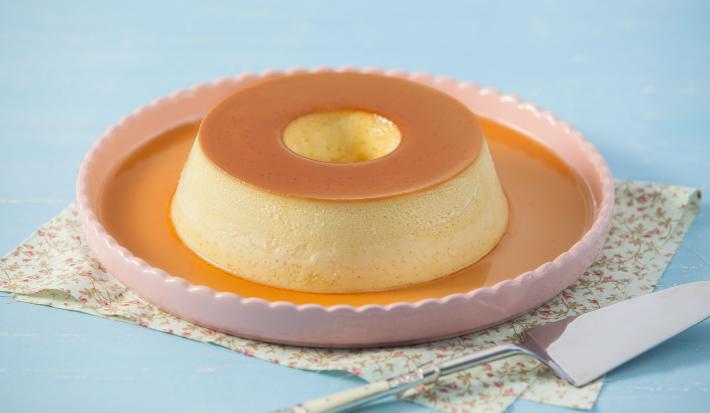Imagem de um prato rosa claro com um pudim de leite condensado moça com calda de caramelo.