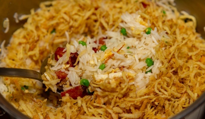 Espátula  cheia arroz com ervilha, pedaços de bacon e batata palha.