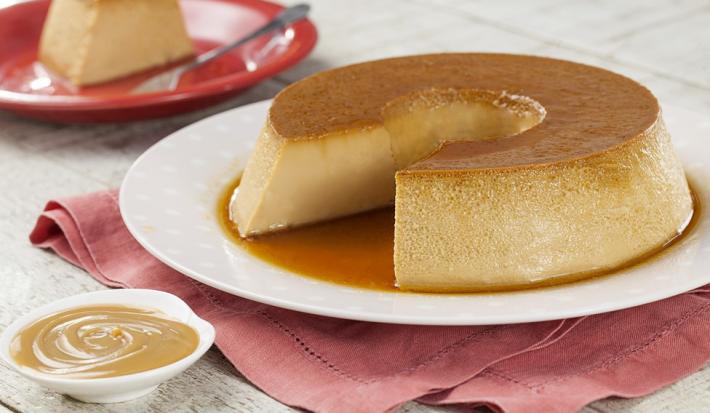 Imagem de um prato branco com o pudim de doce de leite, ao fundo, um prato vermelho com uma fatia.