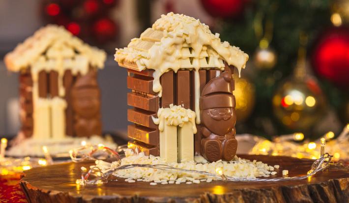 Imagem da receita de Casinha de KitKat Papai Noel, montada num formato miniatura de uma casinha de chocolate em tons marrom e branco, com um Papai Noel de chocolate à frente, sobre uma tábua de madeira e com decorações de natal ao redor Imagem da receita de Casinha de KitKat Papai Noel, montada num formato miniatura de uma casinha de chocolate em tons marrom e branco, com um Papai Noel de chocolate à frente, sobre uma tábua de madeira e com decorações de natal ao redor