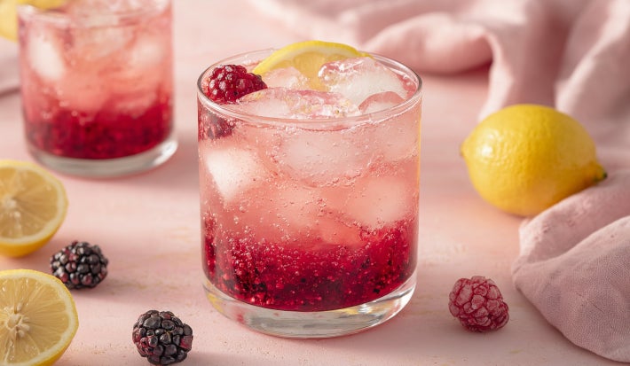 Imagem de um copo transparente com uma bebida com pedaços de frutas vermelhas decoradas com folhas de hortelã