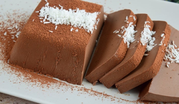Em cima de uma mesa, prato branco com Bavaroise cortados em fatias, decorado com coco ralado.