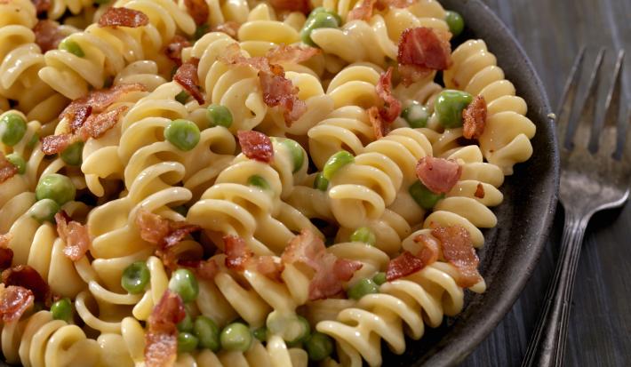 fotografia em tons de preto e bege de uma bancada preta vista de cima. Contém um recipiente preto redondo com macarrão parafuso, pedaços de bacon e ervilhas. fotografia em tons de preto e bege de uma bancada preta vista de cima. Contém um recipiente preto redondo com macarrão parafuso, pedaços de bacon e ervilhas.
