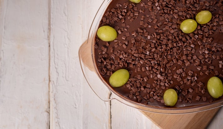 Imagem de travessa de vidro com ganache de chocolate, 
decorada com uvas inteiras e chocolate granulado