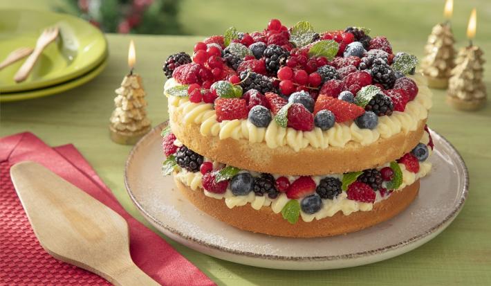 Foto da receita de bolo pelado naked cake natalino sem glúten servida sobre uma base bege em cima de uma mesa verde com decorações de natal, além de um pano vermelho com uma espátula de madeira em cima