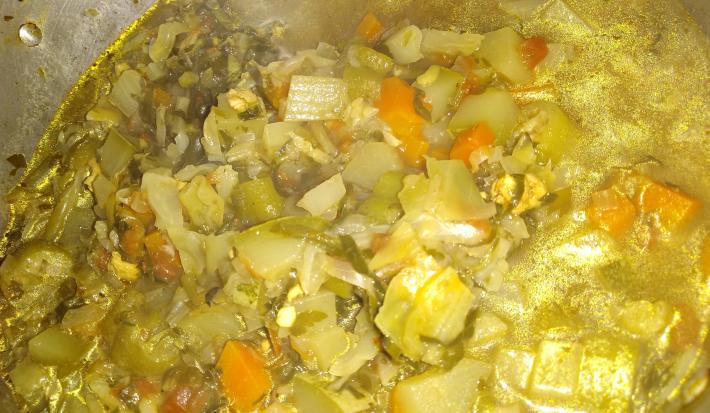 Fotografia de uma panela de alumínio grande com uma sopa de legumes variados.