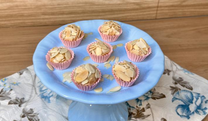Fotografia em tons de azul e rosa com um prato azul ao centro. Em cima do prato, existe 7 brigadeiros de caramelo salgado cobertos com amêndoas laminadas.