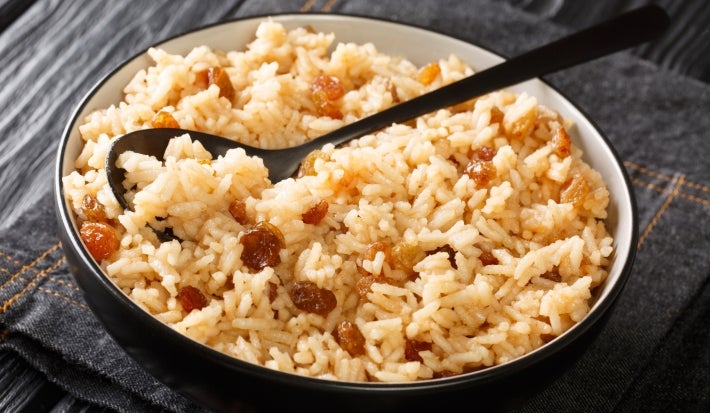 Em cima de uma mesa, tigela redonda com arroz soltinho com uvas-passas brancas.