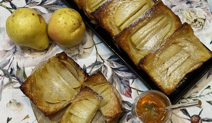 Foto da receita de Folhado de Pera. Observa-se um folhado em forma inglesa com duas peras à esquerda e um potinho de mel na frente,