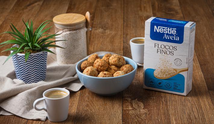 Foto da receita de bolinha crocante de queijo com nestlé aveia disposta em diversas porções dentro de um pote azul claro com um vaso de planta e a embalagem de aveia ao lado
