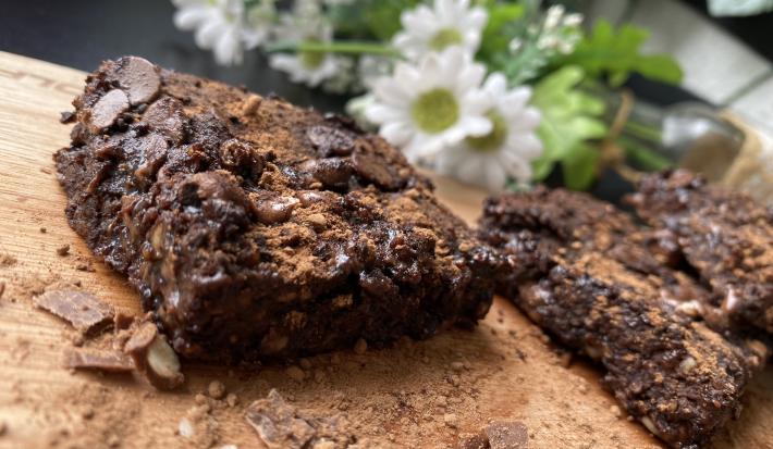 Imagem da receita de Brownie Rápido de Chocolate com Aveia sobre uma mesa e atrás umas flores