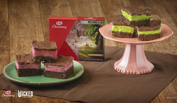 Receita de Brownie Wicked, servidos em pedaços de brownie de chocolate, metade com creme rosa e metade com creme verde, todos cobertos com Chocolate. Alguns em prato verde e outros em um prato rosa alto. No meio há uma caixa de KitKat Wicked.