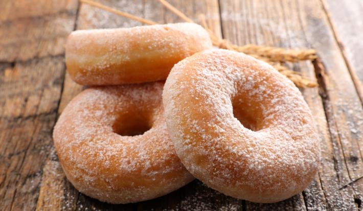 Fotografia de três rosquinhas, uma apoiada na outra, passadas no açúcar de confeiteiro, sobre uma mesa de madeira.