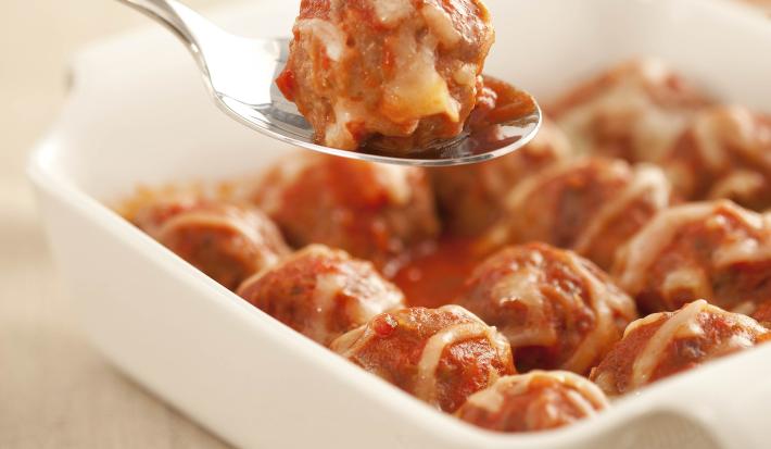 foto em tons de branco e vermelho de uma bancada vista de cima, um recipiente quadrado branco com alças contém bolinhos de carne moída com molho de tomate por cima