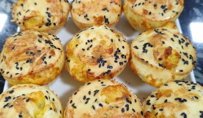 Foto da receita de Pão de Queijo Funcional. Observa-se um prato branco quadrado com 9 unidades de pão de queijo polvilhados de gergelim preto em cima.