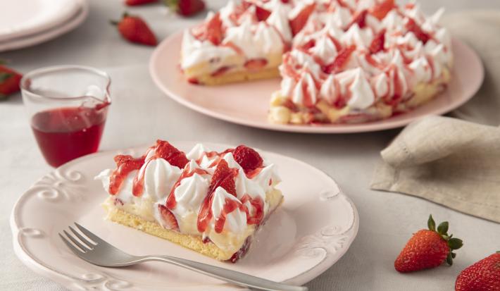Imagem de um prato com uma fatia de torta coberta com merengue, morangos e calda. Ao fundo, uma prato rosa claro com a torta.