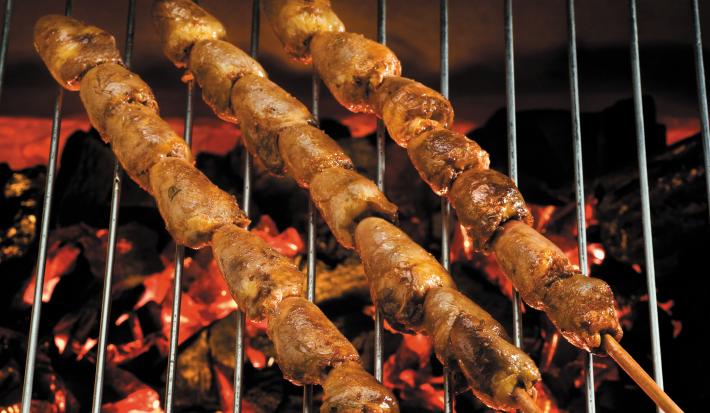 Fotografia de três espetinhos de coração, com sete unidades da carne em cada. Os espetinhos estão um do lado do outro, sobre uma grelha de churrasco com a brasa acesa.