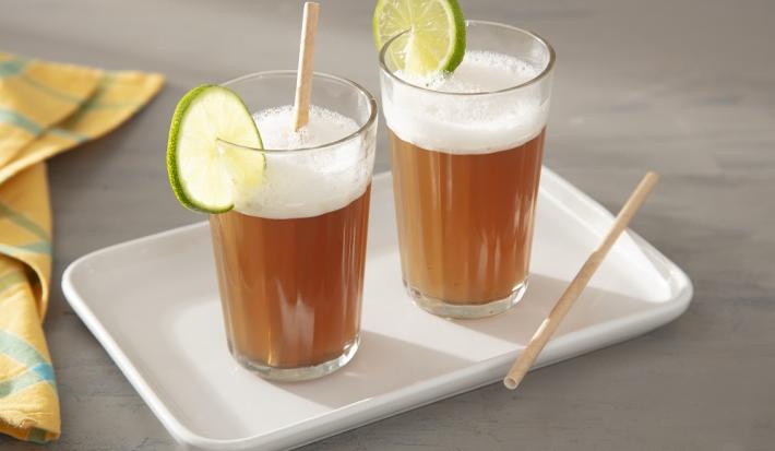 Foto da receita de Suco de Mate com Limão. Observa-se dois copos decorados com uma rodela de limão e com a bebida dentro