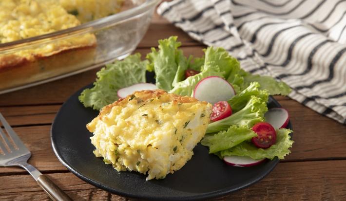 Foto da receita de bolo salgado servida com salada de alface em um prato de porcelana preto sobre uma mesa de madeira com uma espátula prateada ao lado