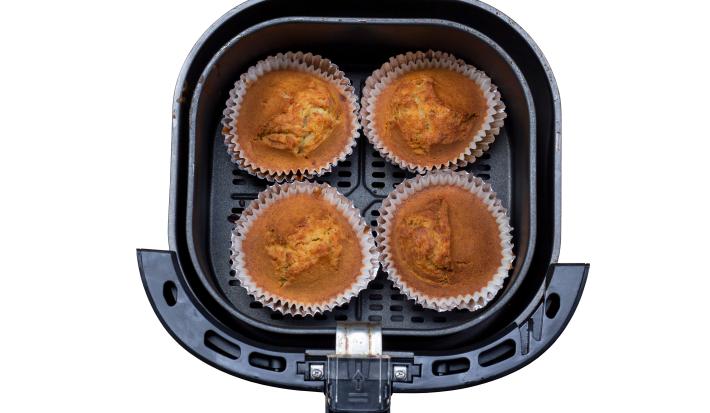Fotografia vista de cima de quatro muffins de banana sem glúten dentro da cestinha da air fryer, a qual está sobre um fundo branco.