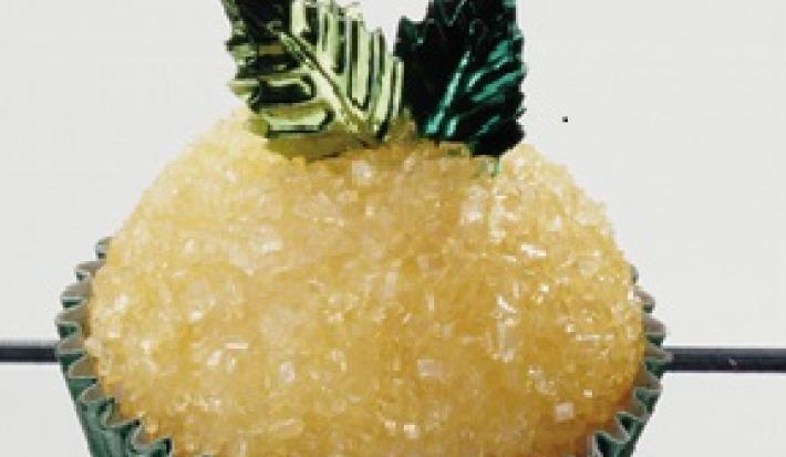 Fotografia em tons de amarelo e verve de um docinho em uma forminha verde, decorado com açúcar e duas folhinhas verdes.
