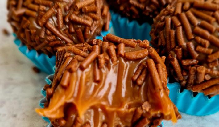 Foto da receita de Brigadeiro Maravilhoso. Observa-se quatro brigadeiros com granulado em forminhas azuis. O da frente está mordido para mostrar a cremosidade.