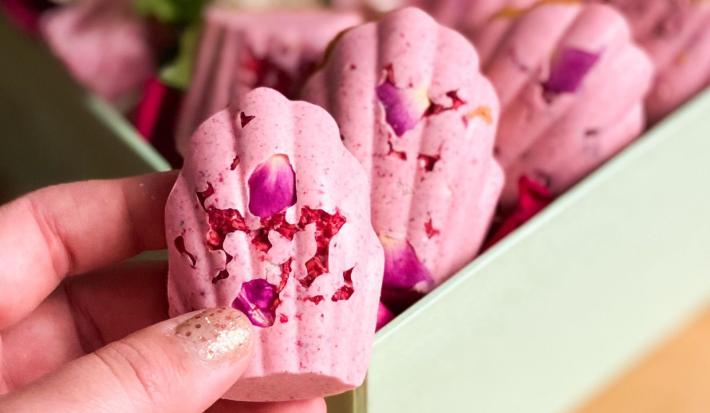 Fotografia em tons de rosa com vários doces cor de rosa ao centro. Esses doces possuem formato de concha e estão dispostos lado a lado.