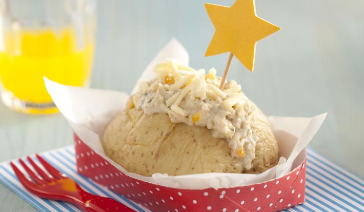 foto em tons de azul, branco e vermelho tirada de um pano listrado em tons de azul e branco. Contém um recipiente vermelho com bolinhas brancas com uma batata e creme de frango por cima e ao lado um garfo para servir