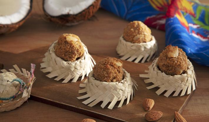 Foto da receita de Cocada com Amêndoas. Observa-se quatro forminhas de chapéu de palha com as cocadinhas em cima. Decoração de festa junina, amêndoas e coco decoram a foto
