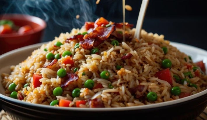 Em cima de uma mesa, tigela com arroz soltinho, bacon picado em pedaços, ervilhas, cenoura picadas, decorado com salsinha picada.