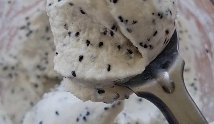 Foto da receita de Sorvete de Pitaya. Obesrva-se uma colher de sorvete com o sorvete de pitaya dentro, branco com sementes, e um pote atrás da colher