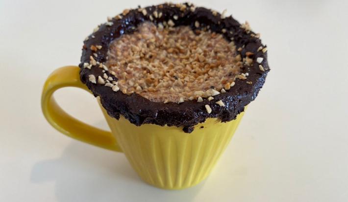 Foto em tons de amarelo da receita de shake de nescau energizante com amendoim servida em uma caneca amarela com cobertura de pasta de nescau e amendoim sobre uma mesa branca