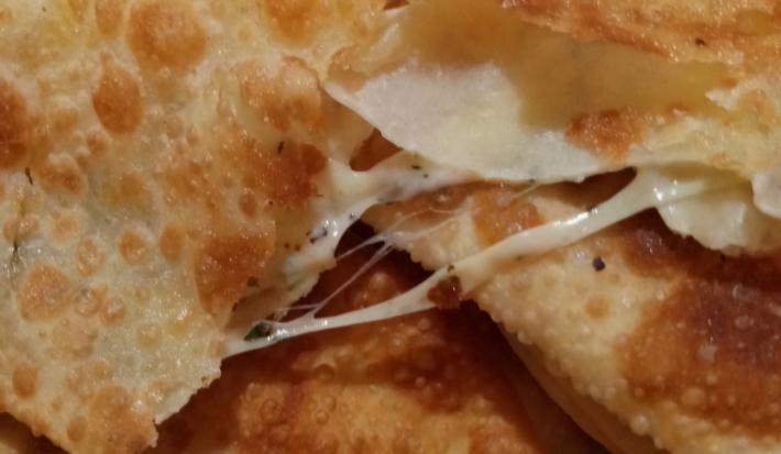 Fotografia de alguns pasteis com creme de calabresa e banana d'água, um sobre o outro. O pastel de cima está cortado na metade com queijo escorrendo.