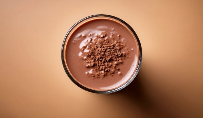Fotografia vista de cima de um copo grande de vidro com a sobremesa natalina, finalizada com ganache e raspas finas de chocolate.