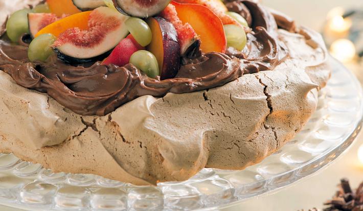 fotografia tirada de frente, contém um suporte para servir sobremesas transparente por cima um merengue coberto de chocolate com frutas para decorar. fotografia tirada de frente, contém um suporte para servir sobremesas transparente por cima um merengue coberto de chocolate com frutas para decorar.